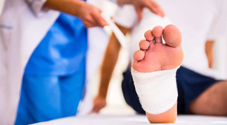 A close-up of a patient's bandaged foot being treated by healthcare professionals, with a focus on the foot and medical staff in the background.