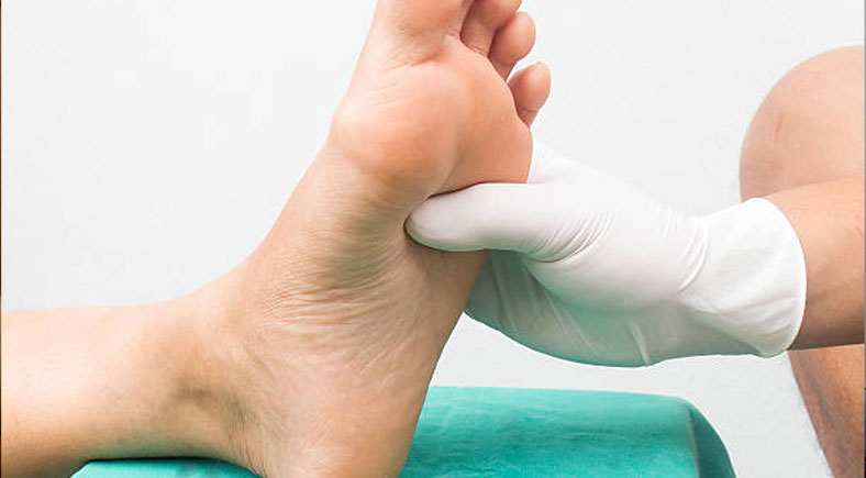 Healthcare professional wearing gloves performing a physical examination of a patient’s foot.