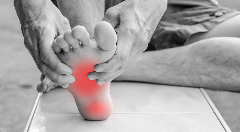 Person holding their foot with visible red highlight indicating pain in the arch area.