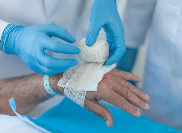Nurse wrapping bandage on elderly patient's hand during wound dressing
